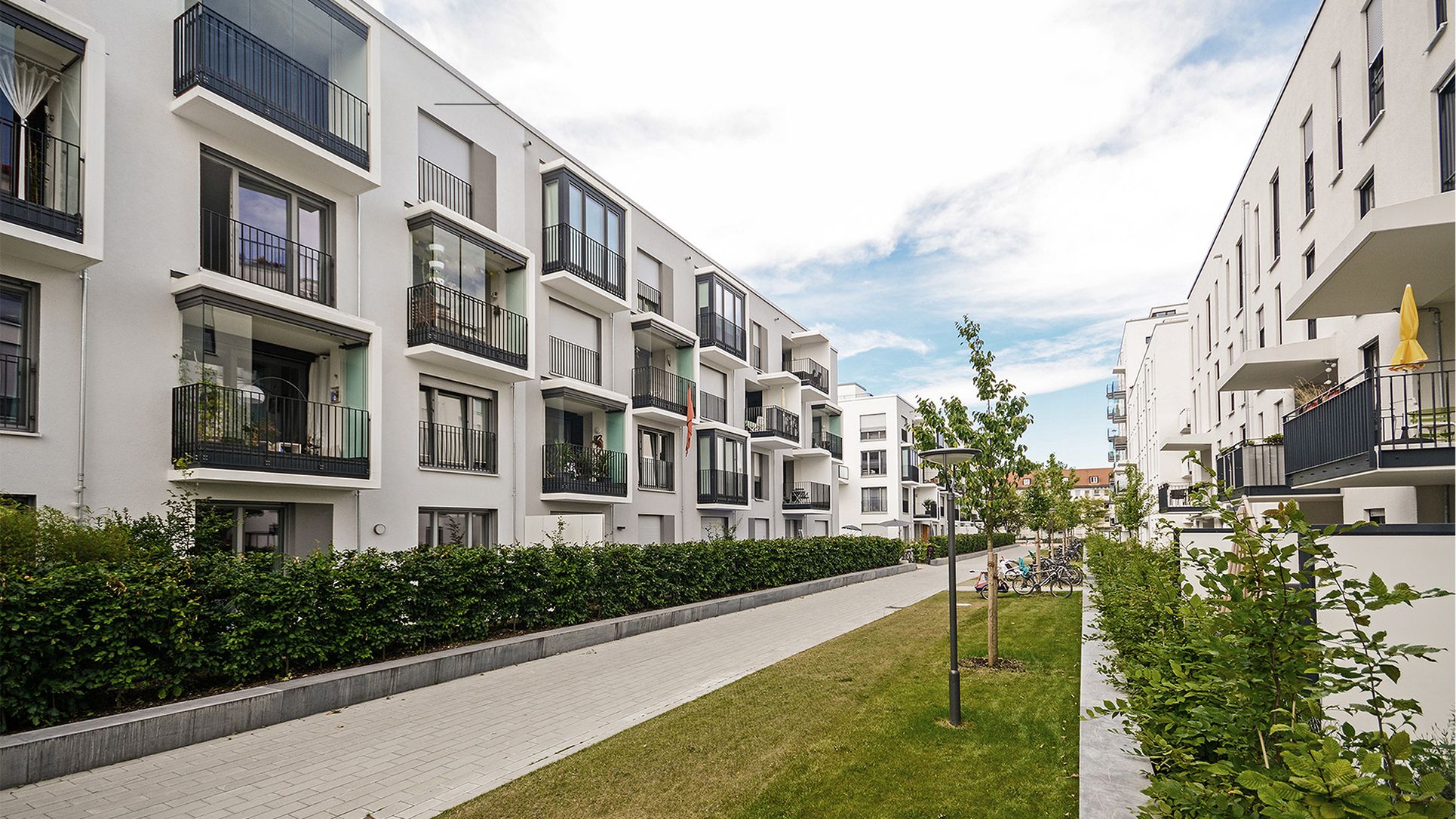Moderne mehrstöckige Wohnanlage mit weißen Fassaden und verglasten Balkonen an einem gepflasterten Gehweg